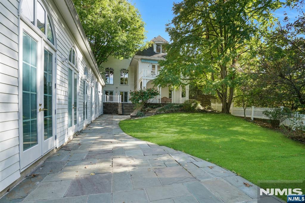 Home exterior with a stone patio beside a lawn shaded by mature trees.
