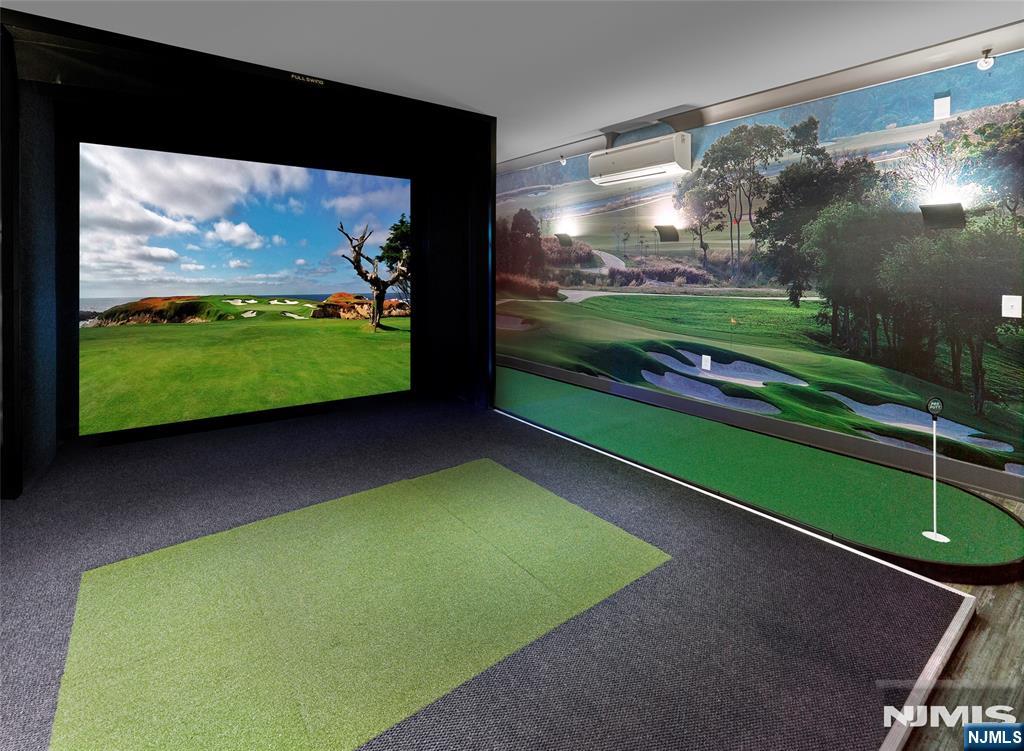 Golf simulator room with a large screen, golf-course mural, and putting turf.