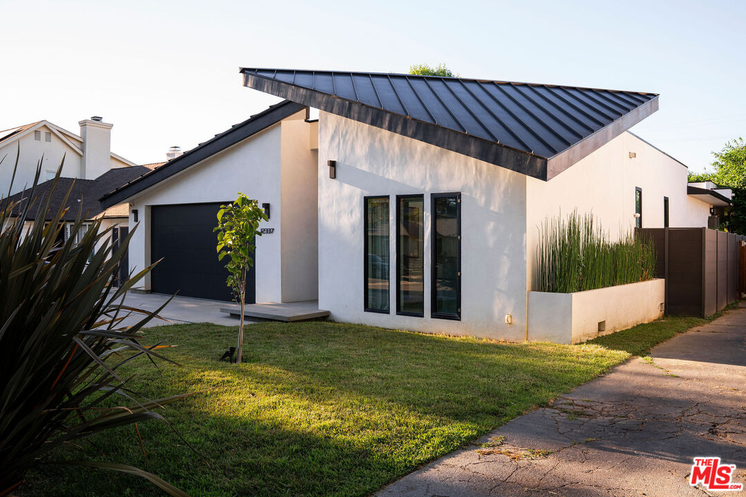 Modern white home with a dramatic black roof, dark garage door, and landscaped front lawn.