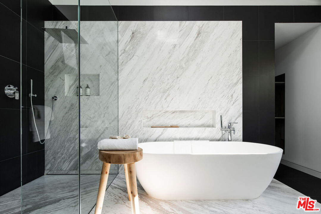 Modern bathroom with a freestanding tub, veined marble walls, and a glass-enclosed shower.