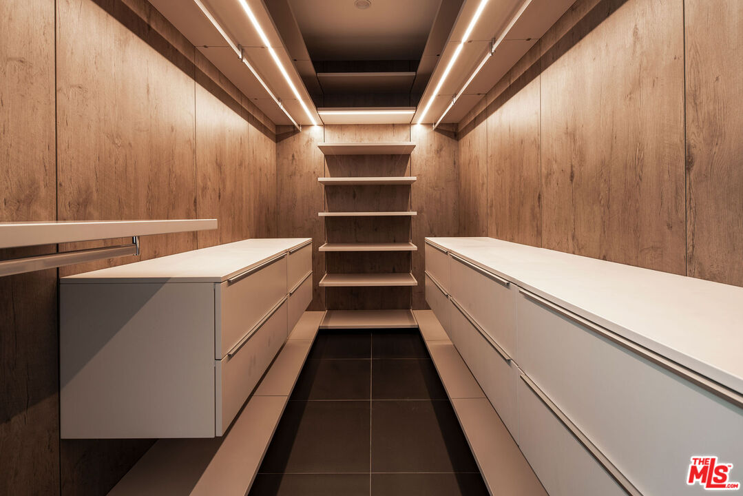 Walk-in closet with illuminated shelving, wood-paneled walls, and white built-in drawers.