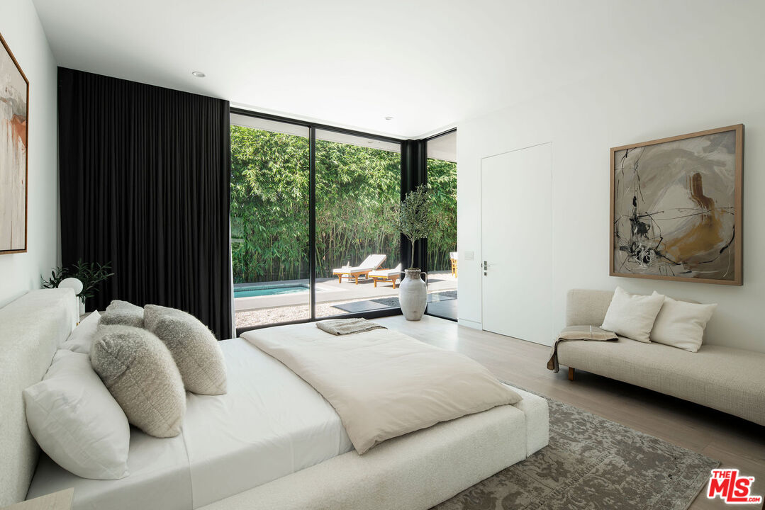 Staged bedroom with a white bed and glass doors overlooking a pool and leafy garden.