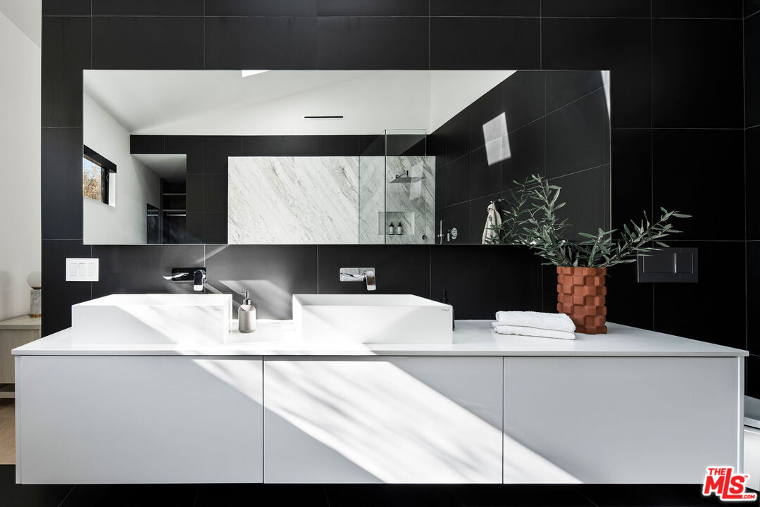 Modern bathroom with a double white vanity, black tile walls, and a mirror reflecting a marble shower.