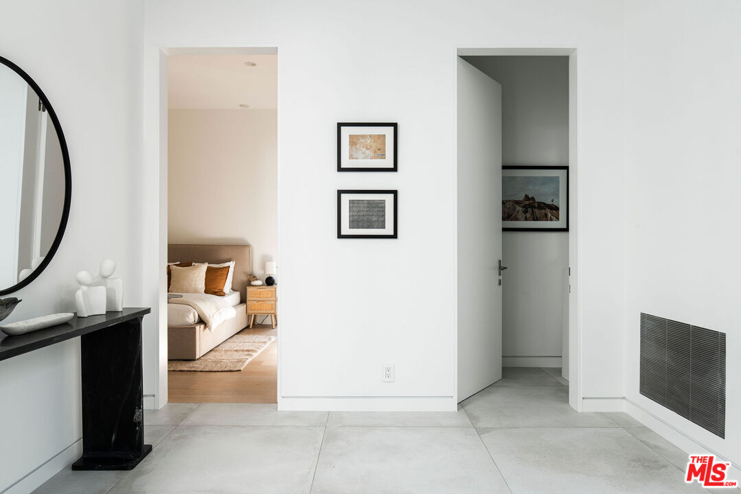 Tiled entry hall with a black console and mirror, opening onto a furnished bedroom.