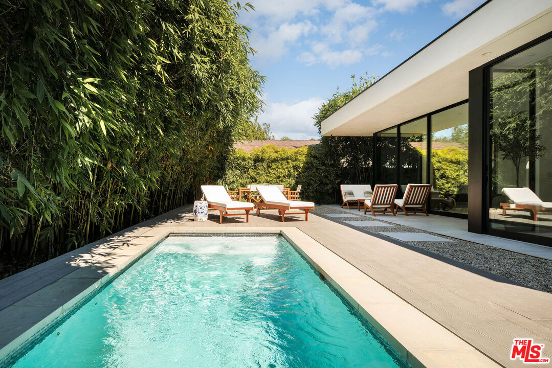 Swimming pool beside a modern home, framed by bamboo hedges and furnished with outdoor lounge chairs.