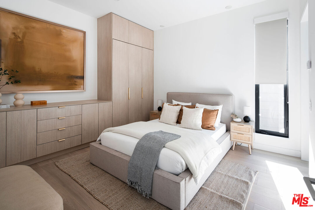 Staged bedroom with a low upholstered bed, built-in light wood cabinetry, and a tall window.