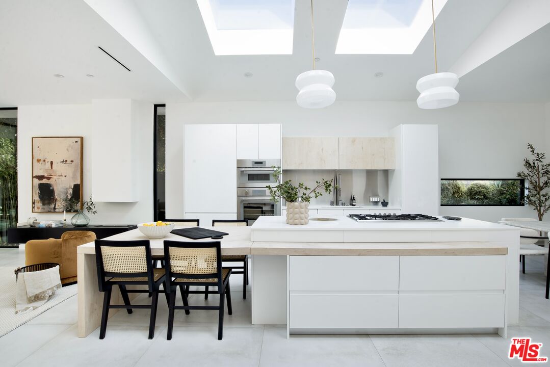Modern white kitchen with a large island, skylights, and an adjoining dining area.