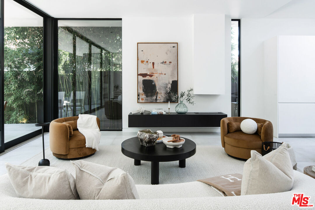 Living room with brown barrel chairs, a black coffee table, and floor-to-ceiling windows overlooking greenery.