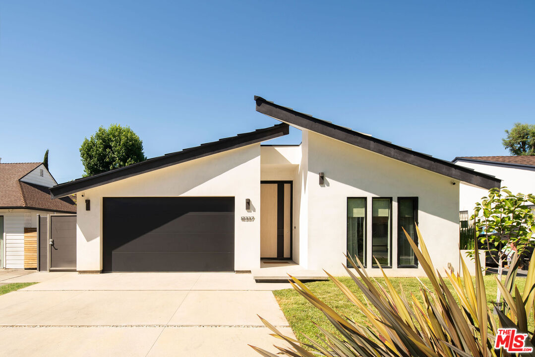 Modern white home with an asymmetrical roof, black garage door, and landscaped front yard.