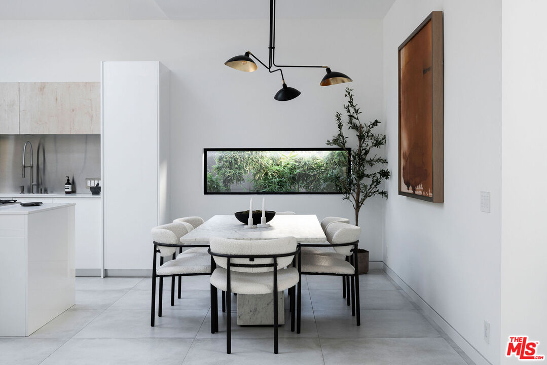 Modern dining area with a marble table, upholstered chairs, and a narrow garden-facing window.