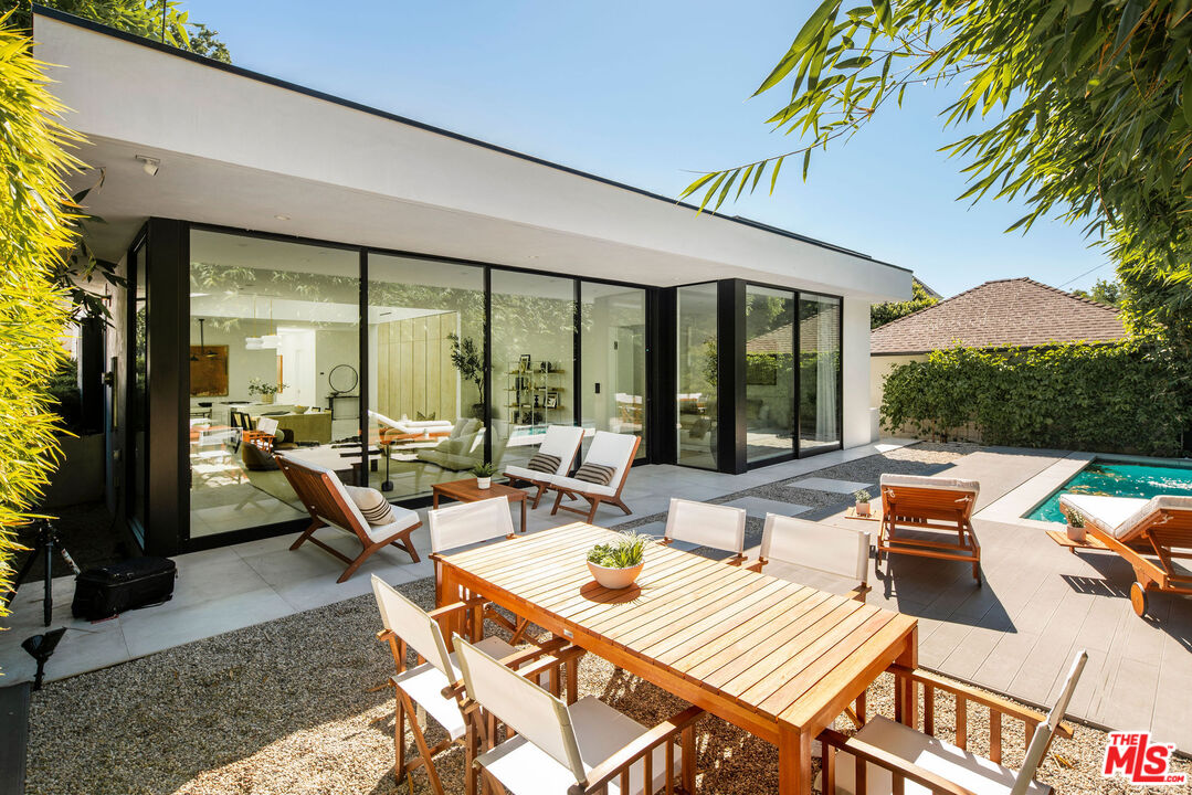 Modern home’s glass-walled patio with a wooden dining table, lounge chairs, and swimming pool.