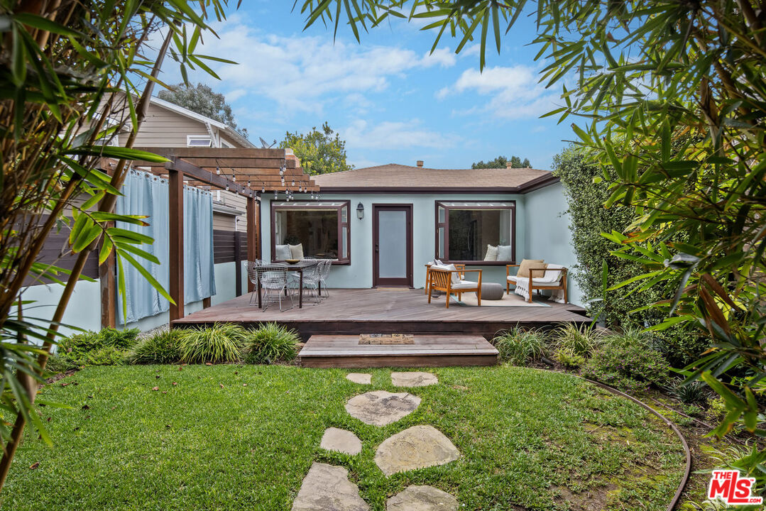Home’s backyard with a raised deck, pergola, outdoor seating, and stepping stones across the lawn.