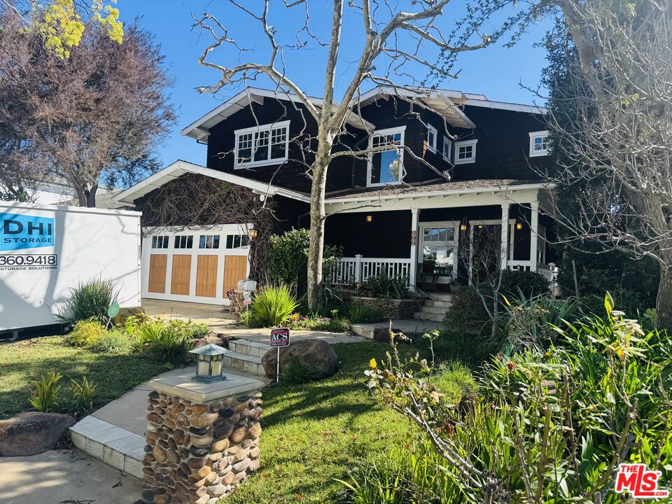 Dark two-story house with a covered porch, wooden garage panels, and a landscaped front yard.
