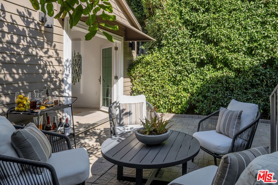Furnished stone patio with cushioned seating, a round table, and a tall privacy hedge.