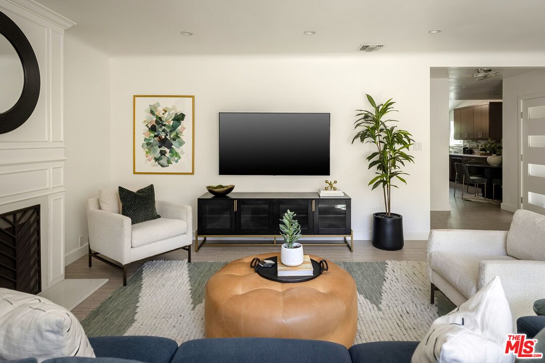 Living room with a black media console, fireplace, and tan ottoman.