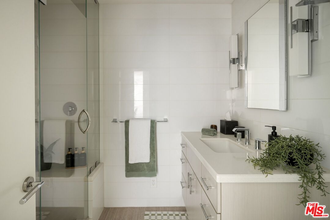 Bright bathroom with a glass-enclosed shower and a long white vanity topped with a potted plant.