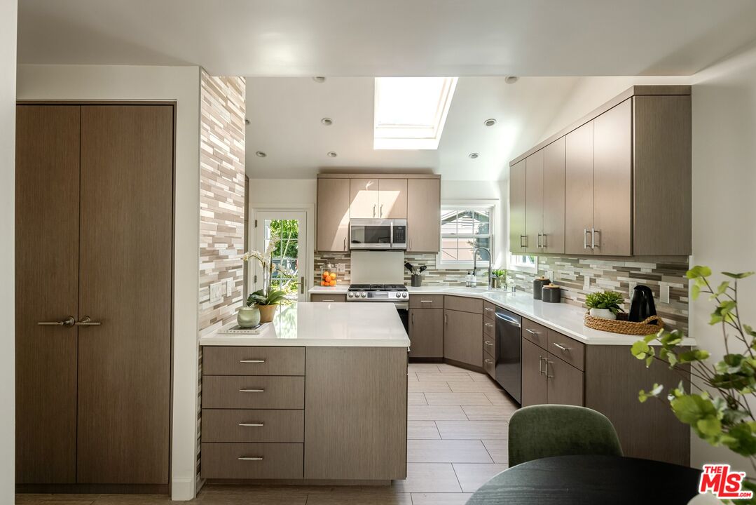 Kitchen with taupe cabinets, a white island, patterned backsplash, and skylight.