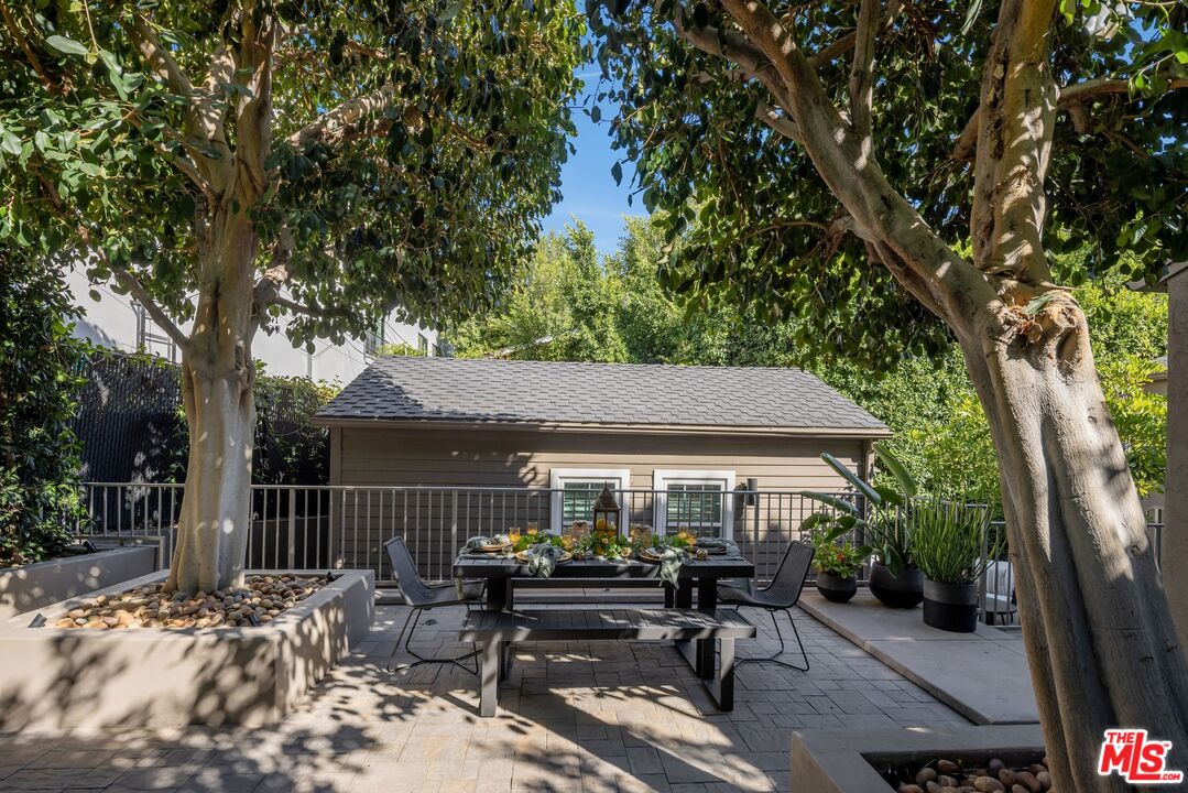 Stone-paved patio with a set outdoor dining table beneath mature trees.