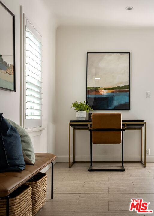 Home office nook with a desk, leather chair, abstract artwork, and a window with white shutters.