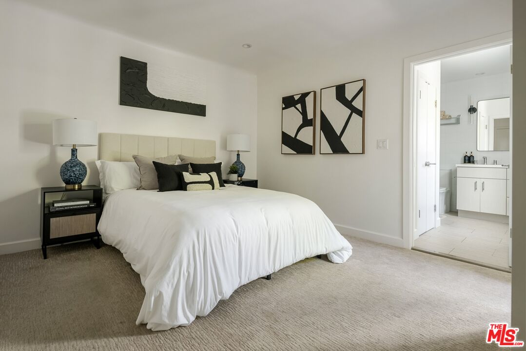 Staged bedroom with a white bed, black-and-white artwork, and an open doorway to the bathroom.