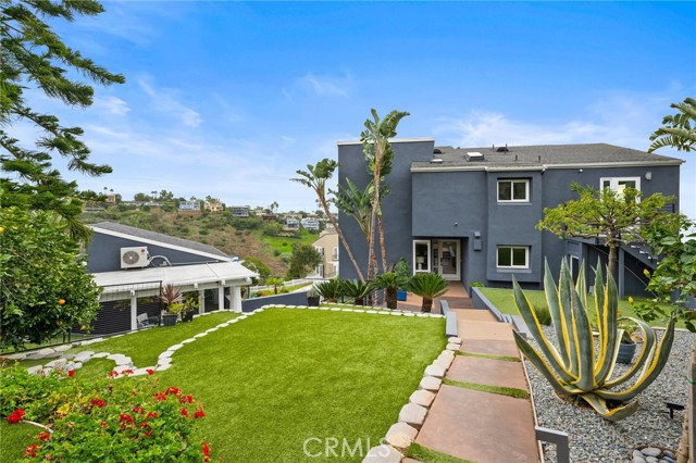 Modern gray two-story house behind a green lawn and stone-edged walkway, with large succulents beside the path.