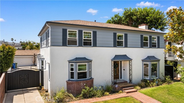 Two-story gray house with dark shutters, a brick-trimmed bay window, and gated driveway.