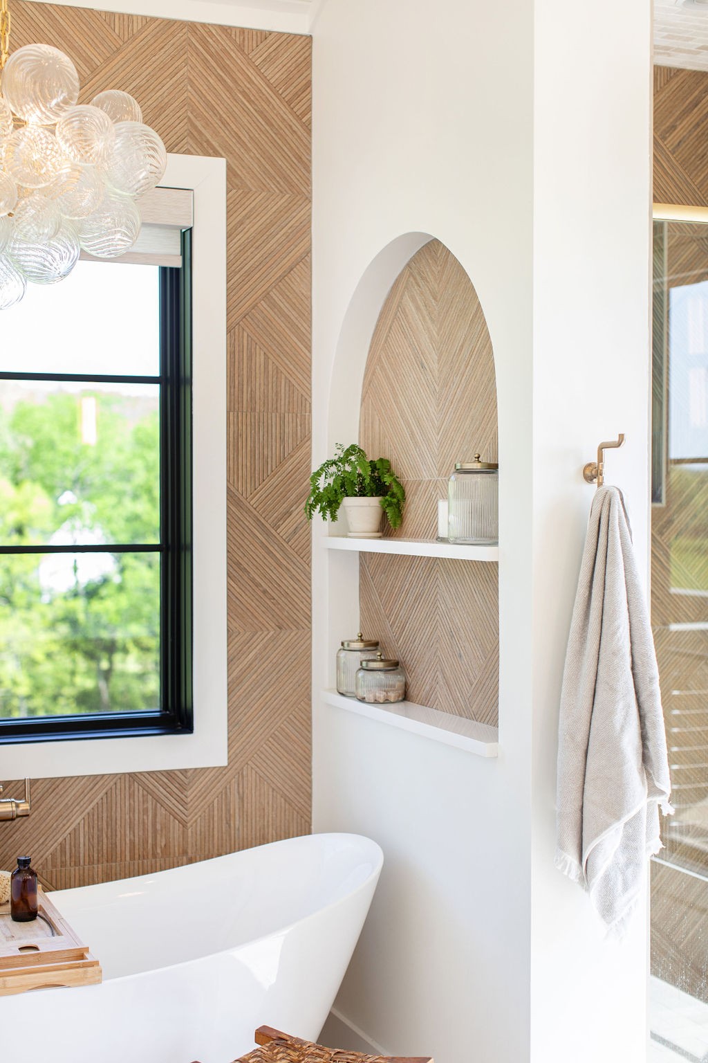 Bathroom with a freestanding tub, arched display shelves, and warm geometric tile.