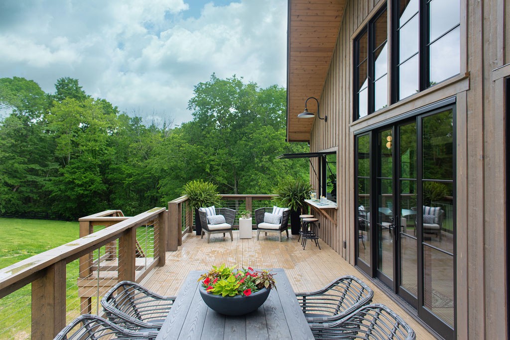 Wooden deck with outdoor dining and lounge seating beside a wooded lawn.