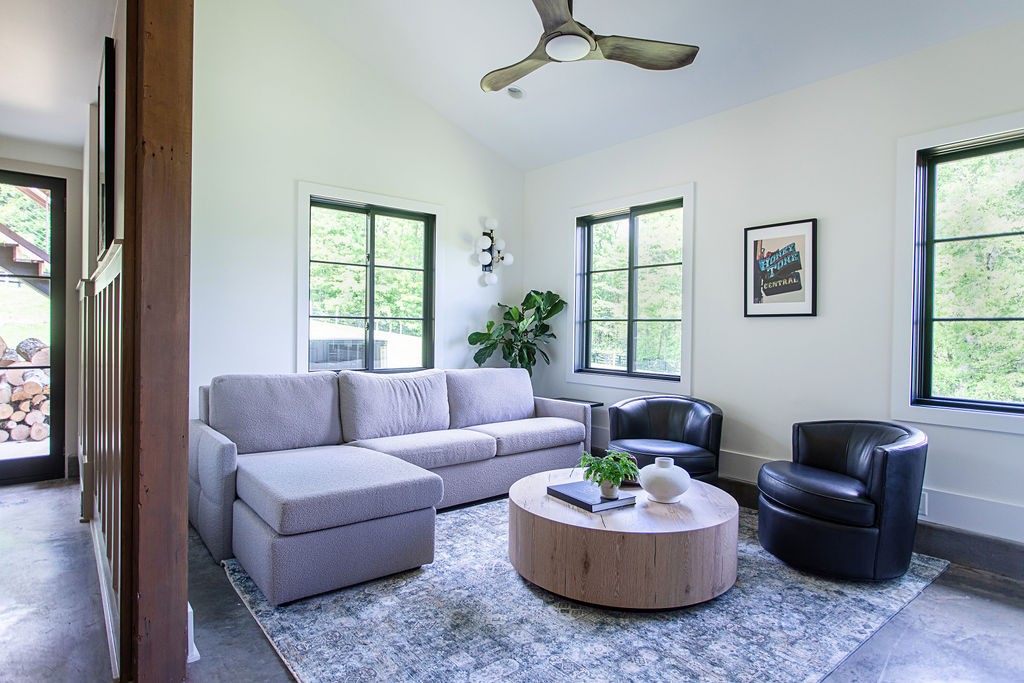Living room with a gray sectional, black leather chairs, round wood coffee table, and large windows.