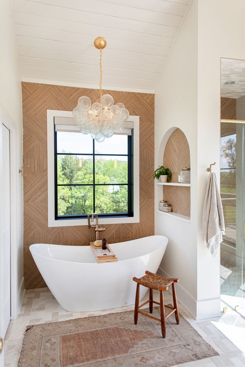 Freestanding soaking tub beneath a black-framed window, backed by a geometric wood accent wall.