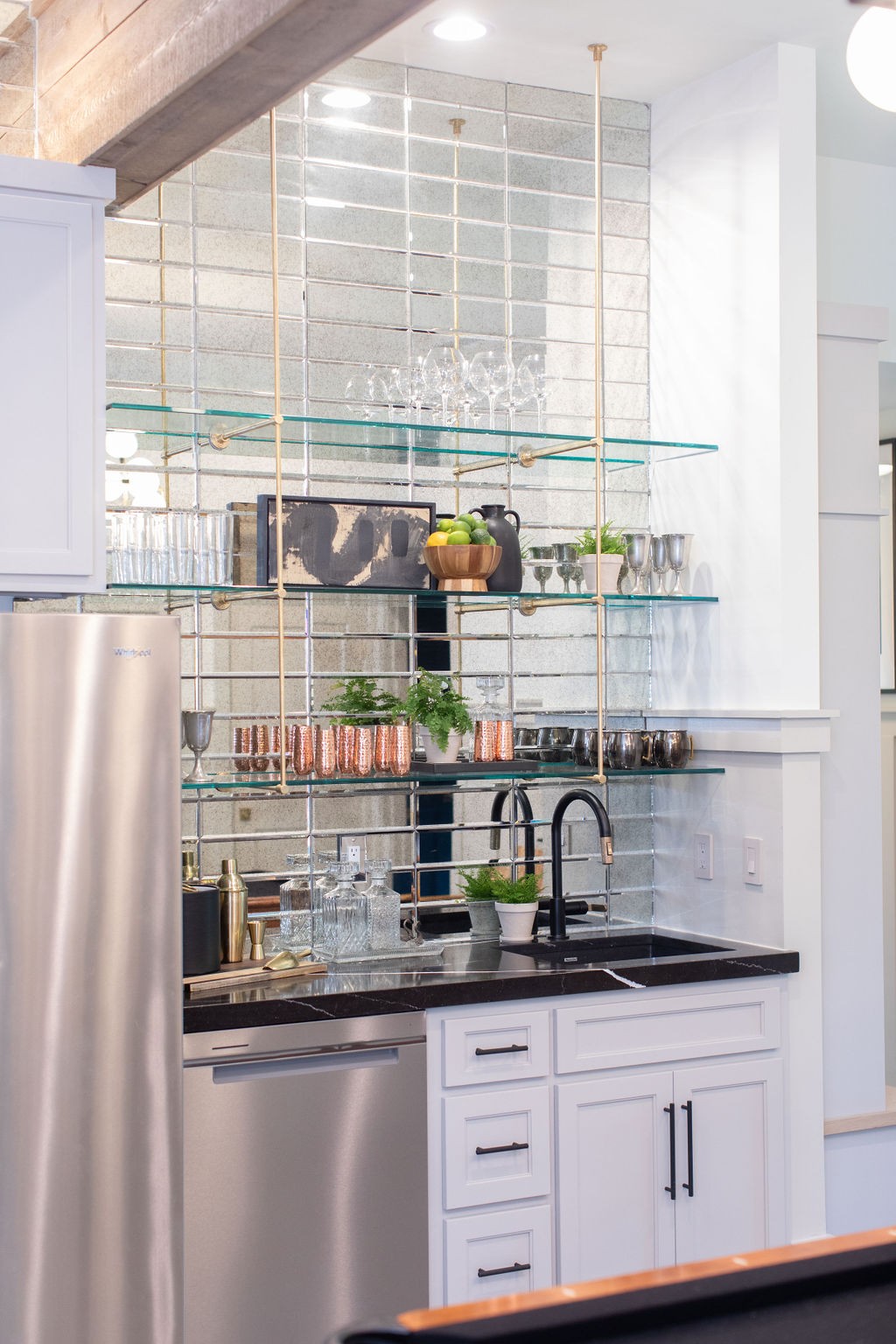 Kitchen beverage area with mirrored tile backsplash, glass shelves, and a black stone counter.
