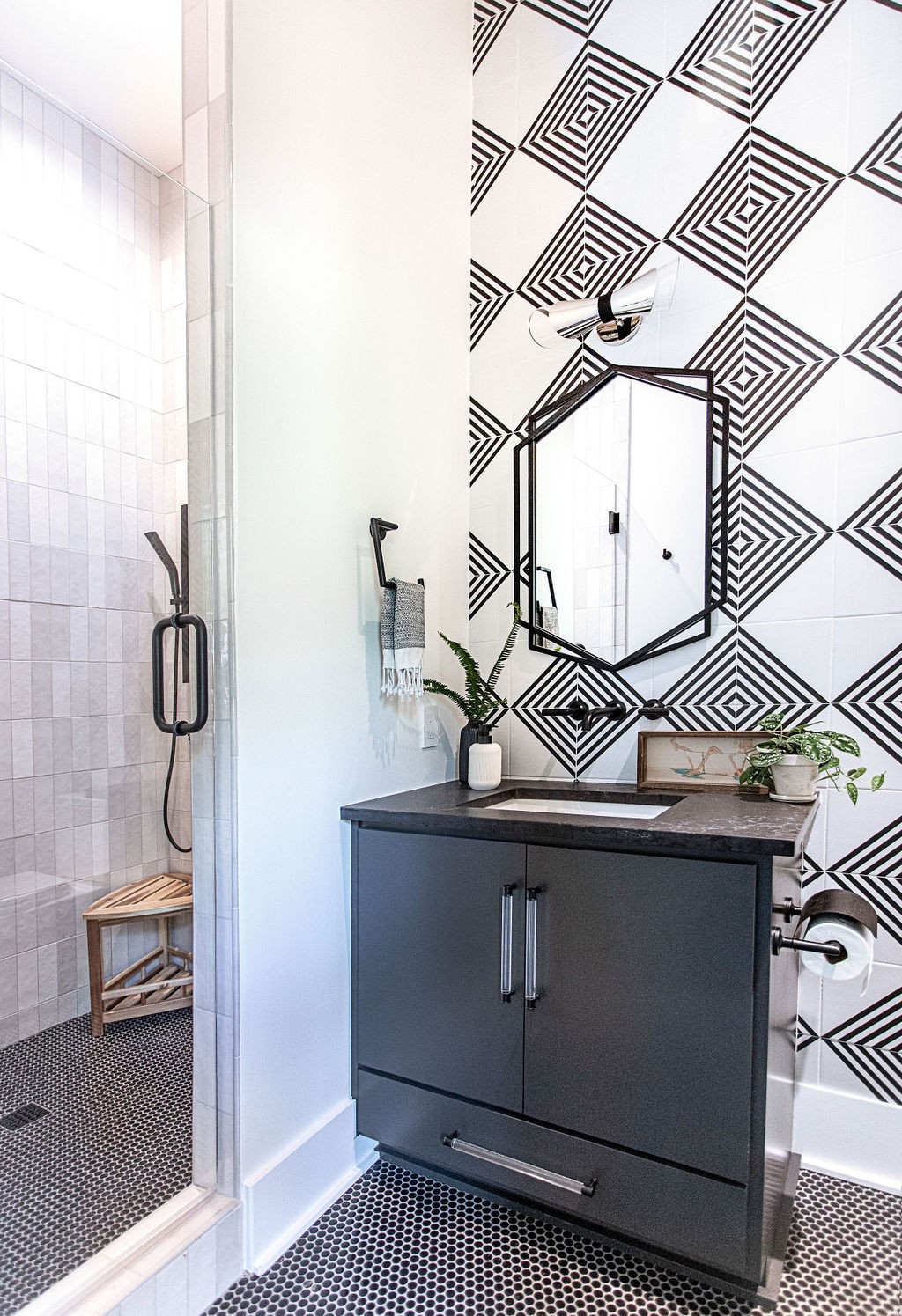 Modern bathroom with geometric black-and-white tile, glass shower, and charcoal vanity.