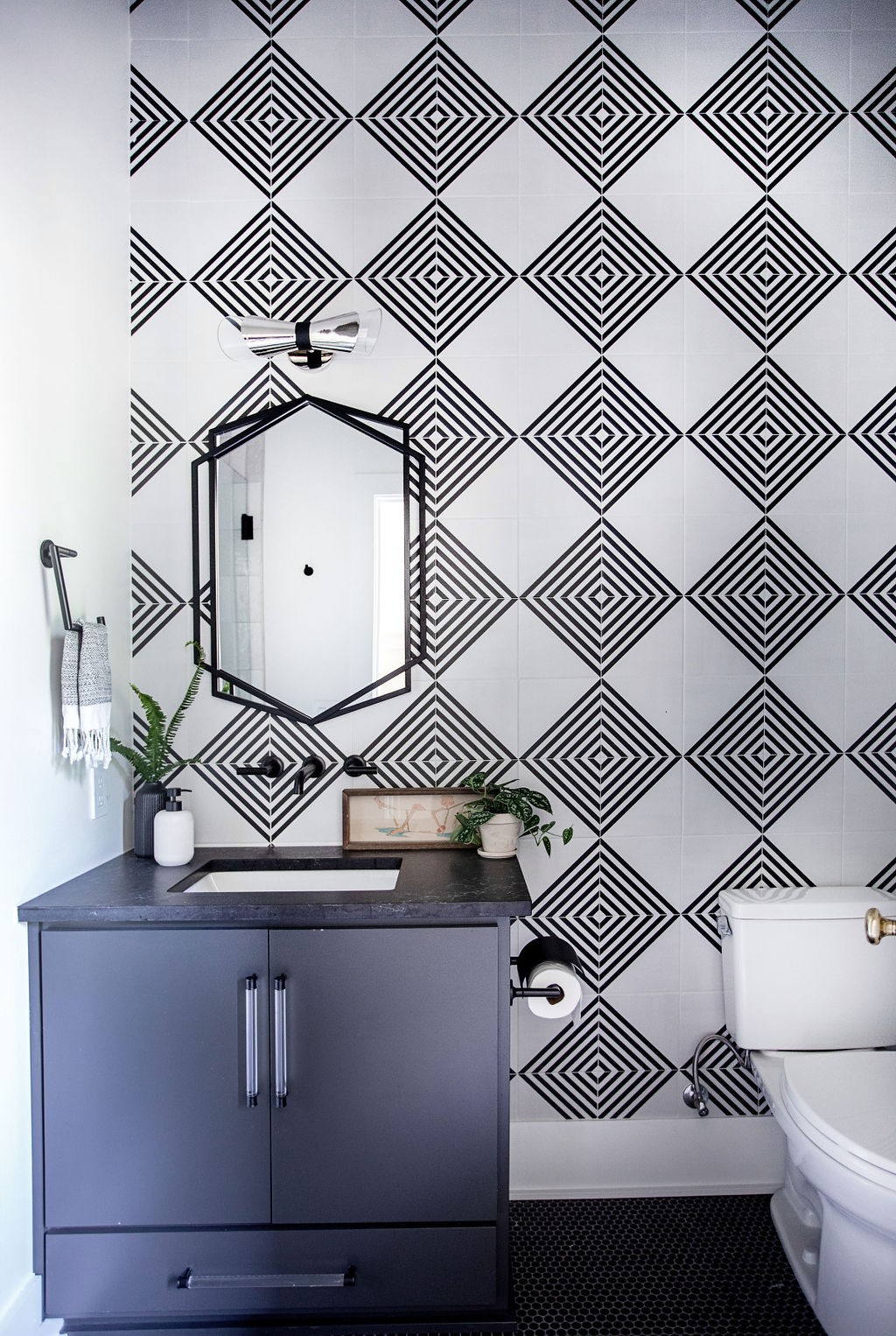 Bathroom with a gray vanity, geometric black-and-white tile wall, and black-framed mirror.