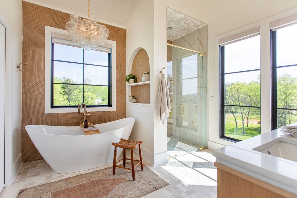 Bathroom with a freestanding soaking tub, herringbone wood accent wall, and glass shower beside large windows.