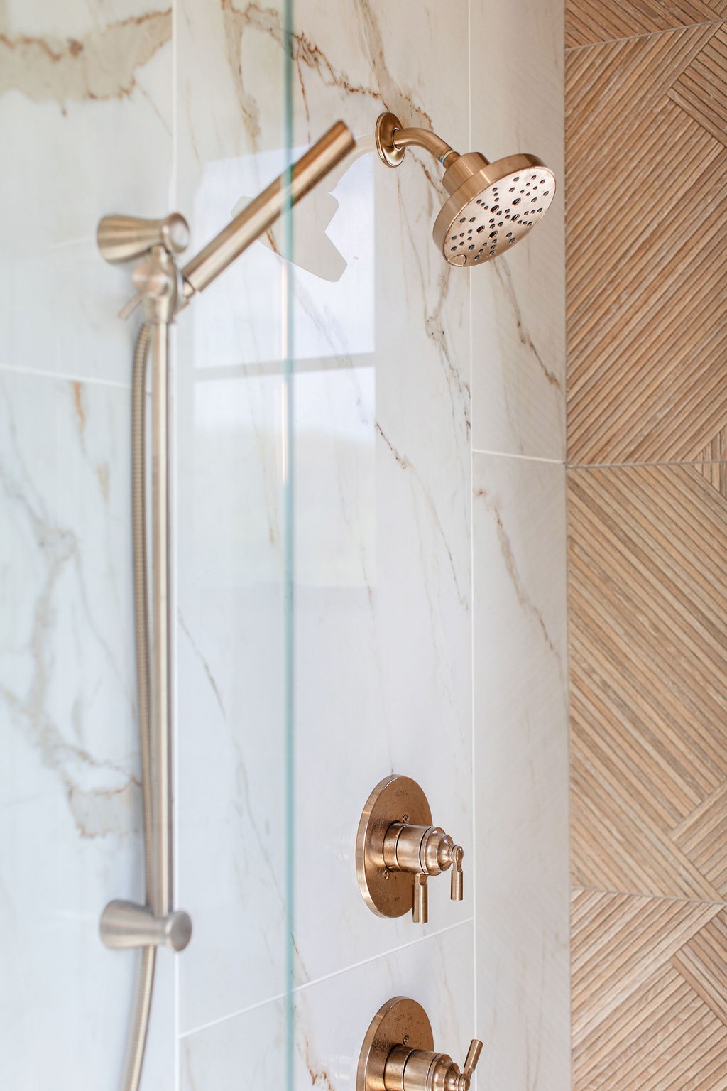 Bathroom shower with bronze-toned fixtures, marble-look tiles, and a herringbone accent wall.