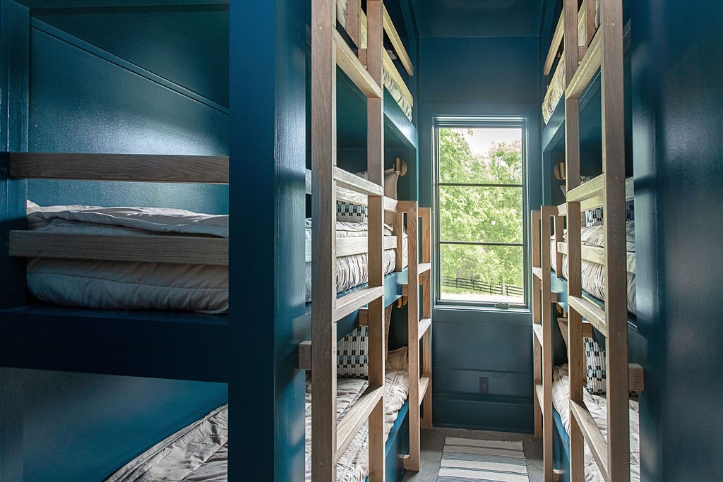 Bunk room with wooden bunk beds, teal walls, and a large window overlooking trees.