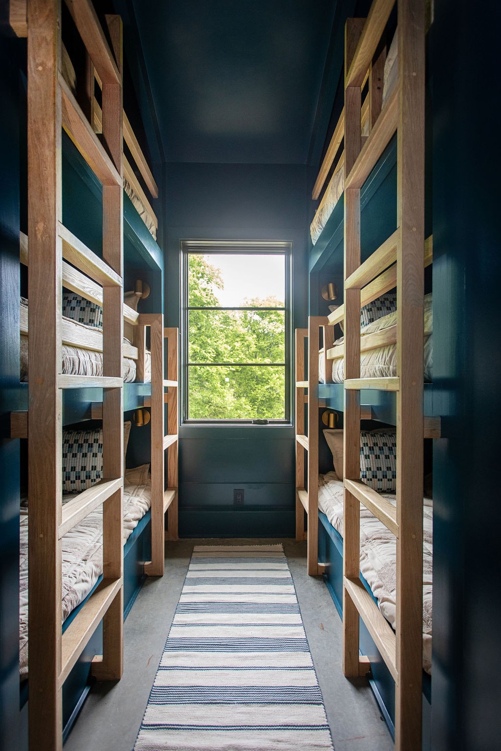 Bunk room with wooden beds on both sides and a large window overlooking trees.