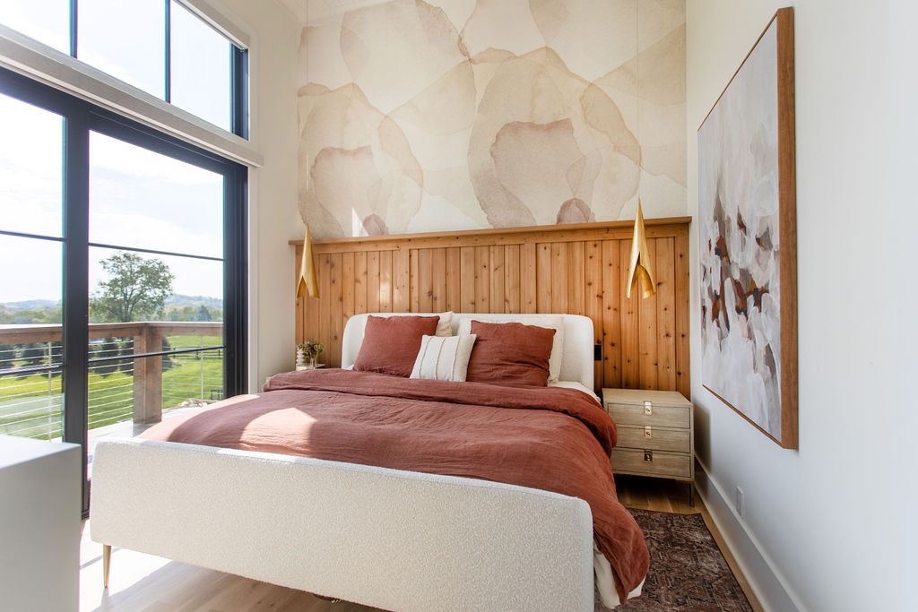Bedroom with rust-colored bedding, a wood-paneled headboard wall, and large balcony windows.
