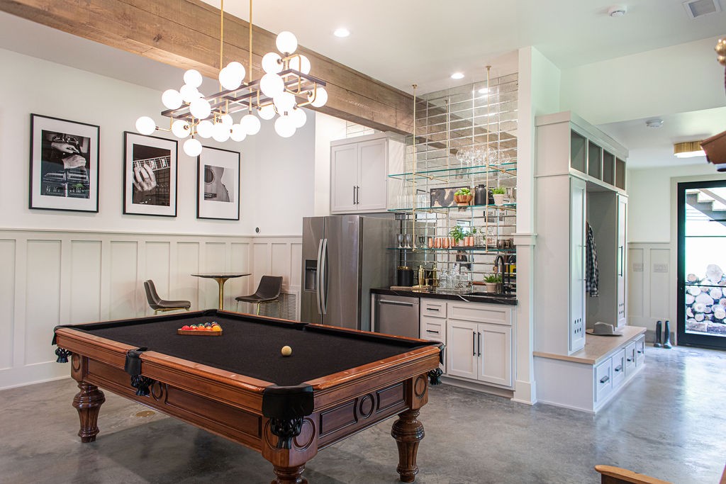 Game room with a pool table, sculptural chandelier, and kitchenette with stainless steel appliances.