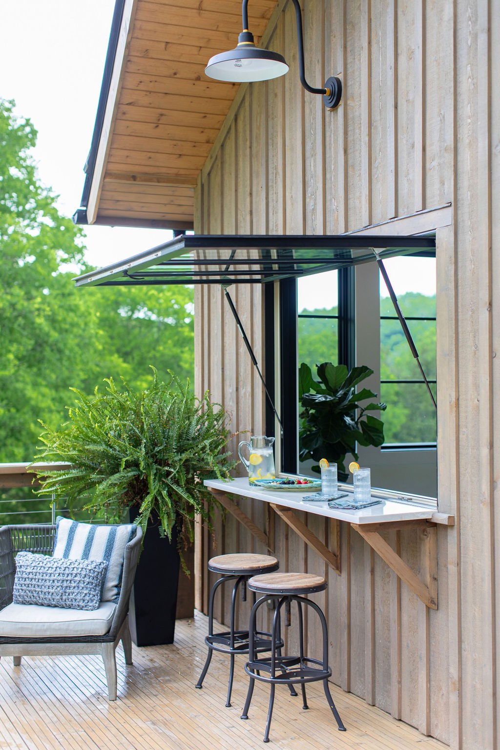 Outdoor patio with a serving counter, awning window, bar stools, and wooded views.
