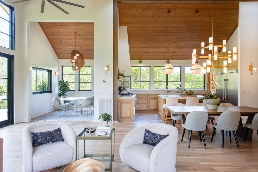 Open-plan living and kitchen area with a wood-plank ceiling, large windows, and a long dining table.