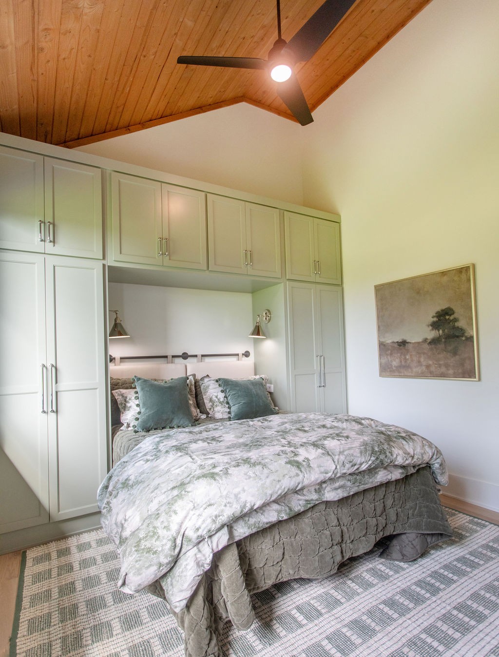 Furnished bedroom with built-in cabinetry, a vaulted wood ceiling, and pale patterned bedding.