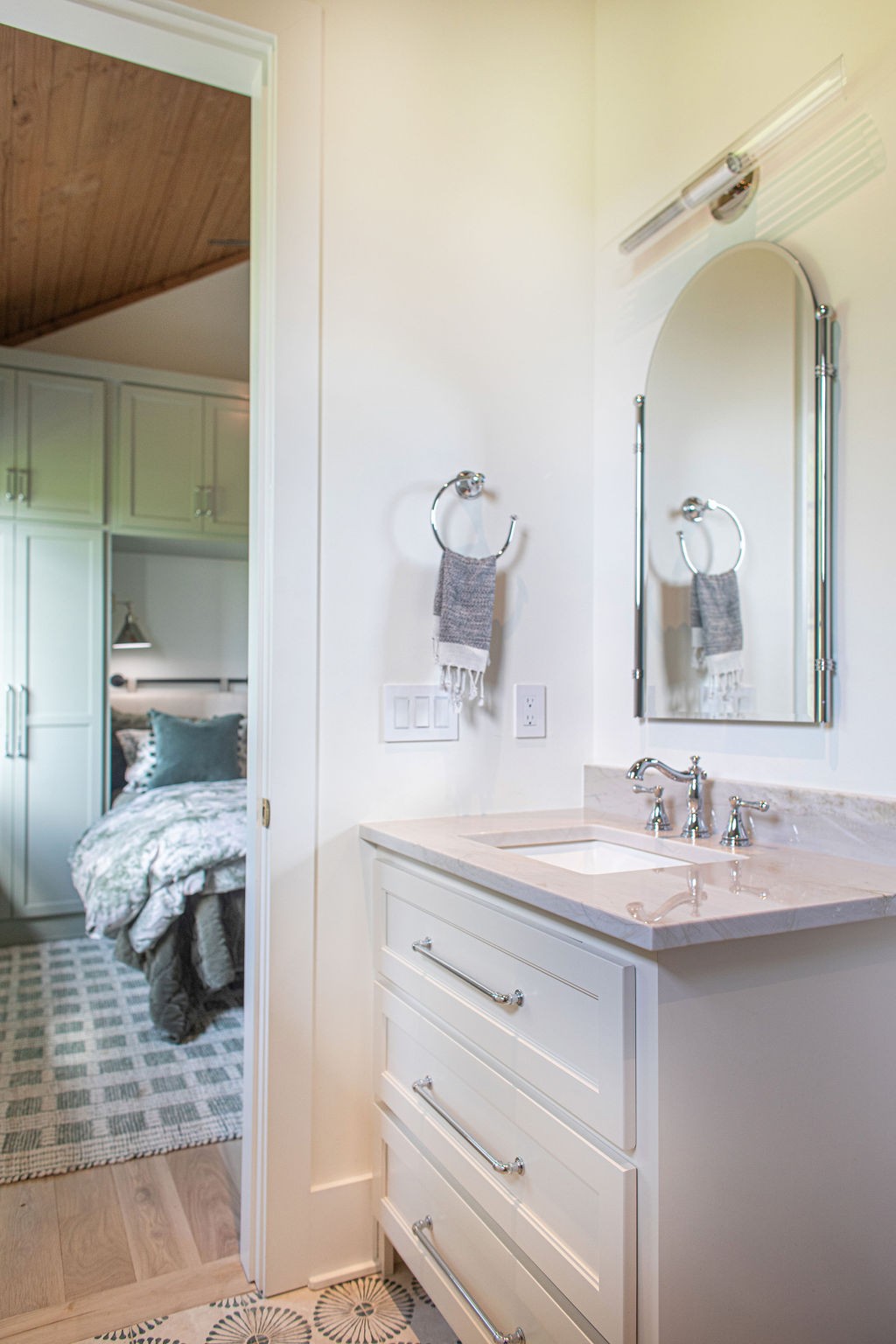Bathroom vanity with marble countertop and arched mirror, opening onto a bedroom.