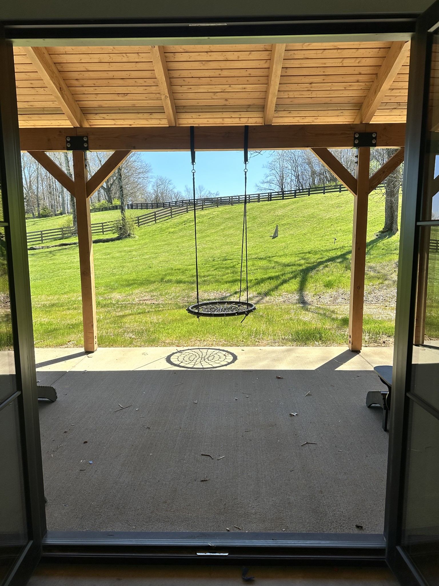 Covered patio with a hanging swing overlooking a sunny, fenced lawn.