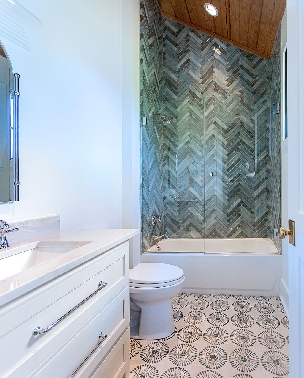 Bathroom with a gray herringbone-tile shower, wood-paneled ceiling, and patterned floor.