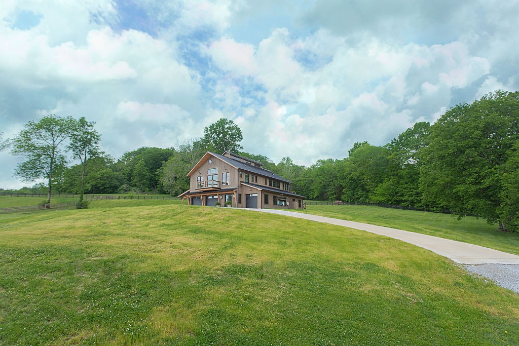 Modern wood-sided house beyond a broad lawn, with a curved driveway and mature trees.