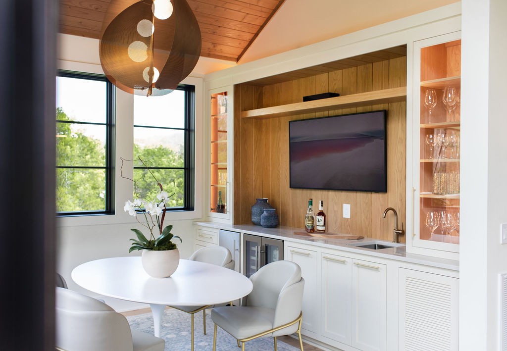 Dining area with built-in bar cabinetry, beverage refrigerators, and large windows overlooking trees.