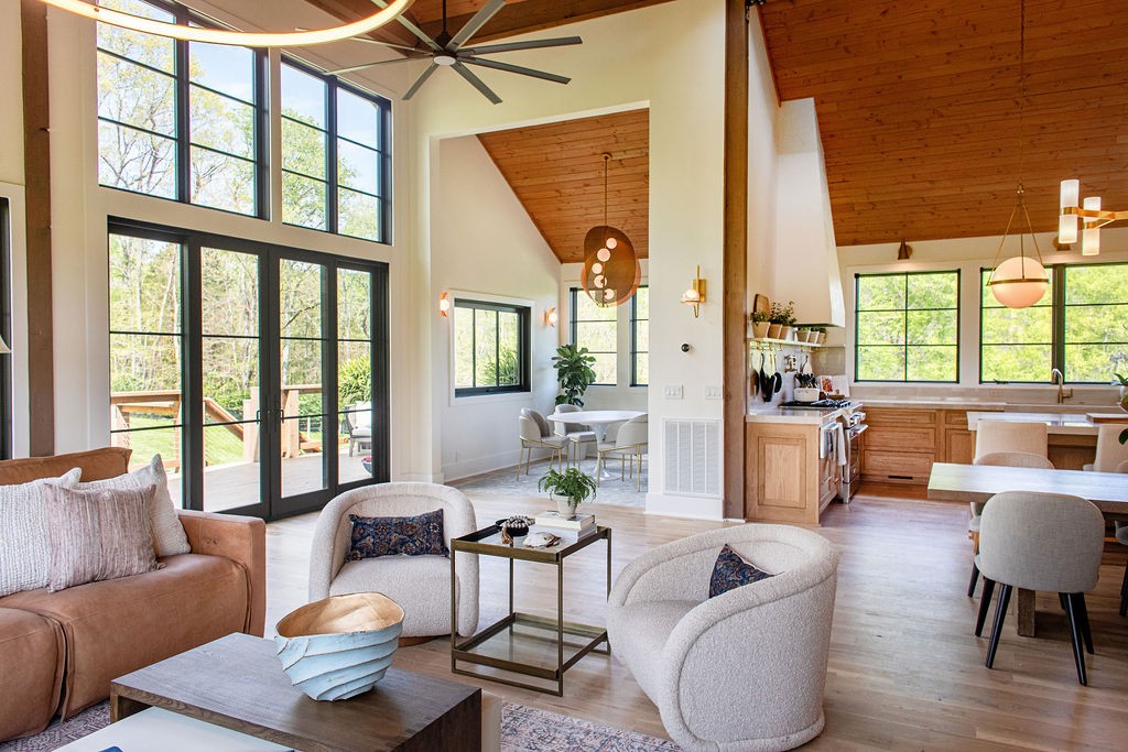 Open-plan living room with vaulted wood ceilings, tall windows, and glass doors to a deck.