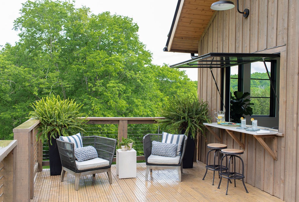 Outdoor deck with cushioned chairs, a built-in counter, and a wooded view.