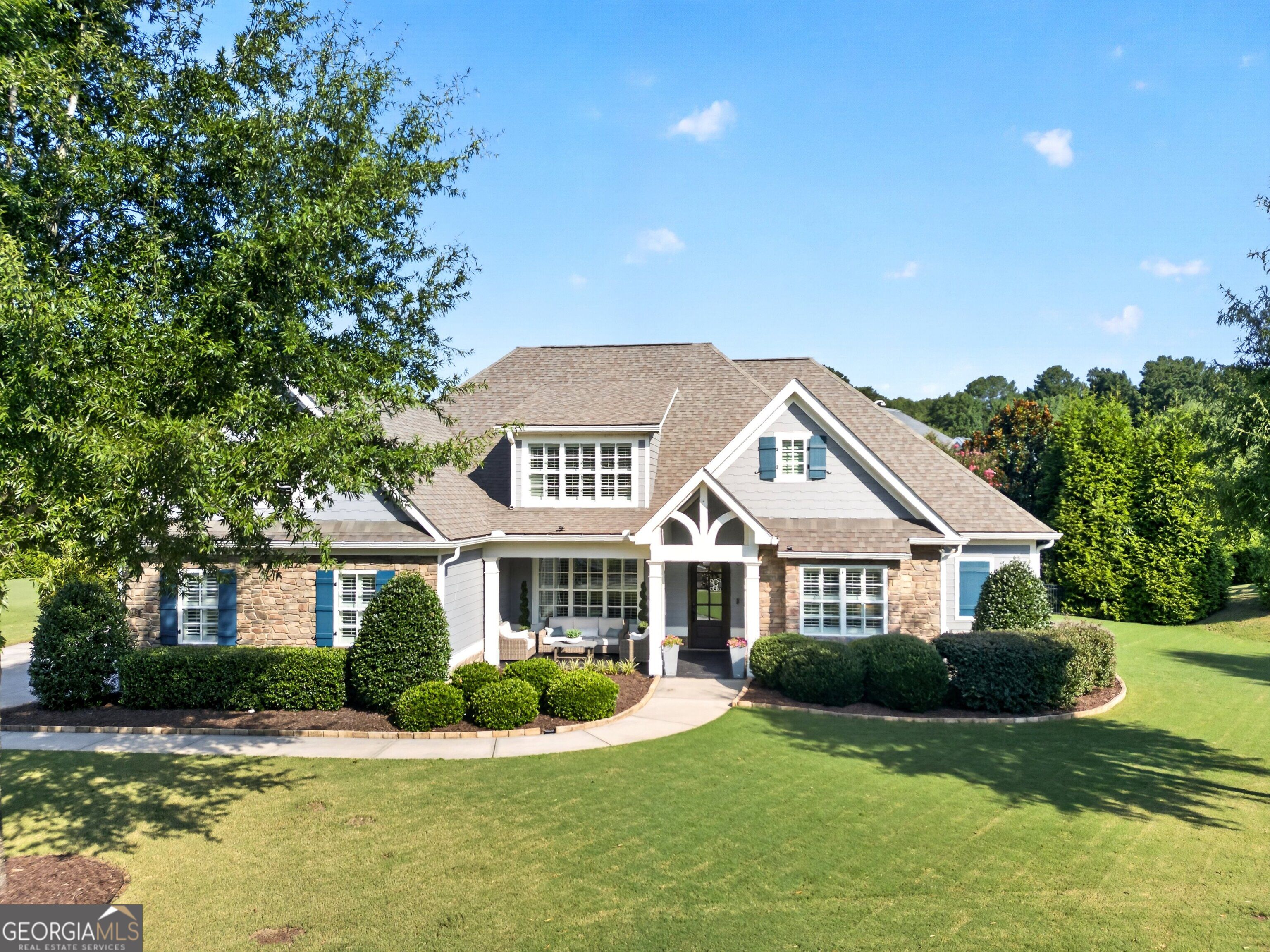Two-story stone-and-siding home with blue shutters, a covered entry, and a broad front lawn.